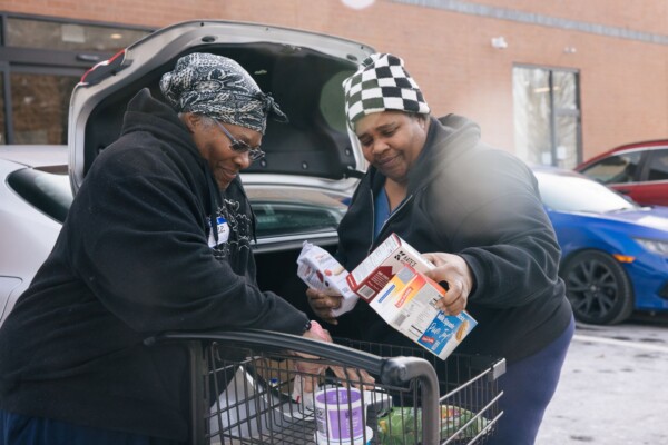 Two guests load food from a grocery cart into their car.