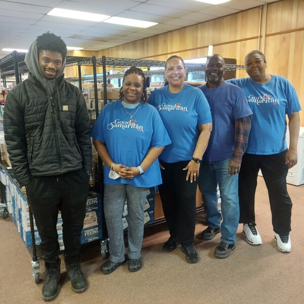 Four people wearing blue t shirts (and one man in a black winter jacket) smile at the camera.