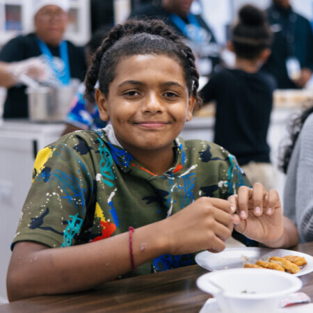 A young boy named Tyleeq eats chicken nuggets from a plate and smiles at the camera.