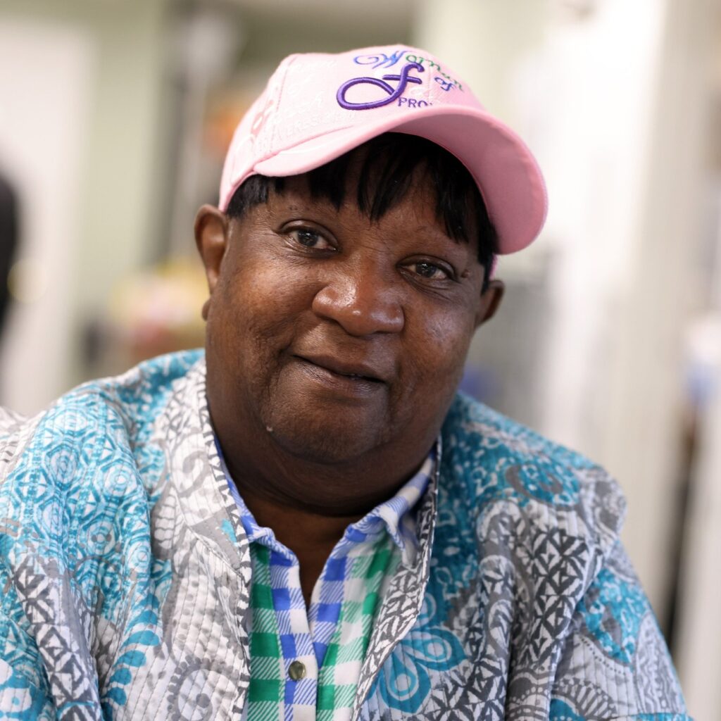 A closeup image of Vanessa: She looks forward with her head tilted slightly. She wears a pink baseball cap and a blue, patterned shirt.