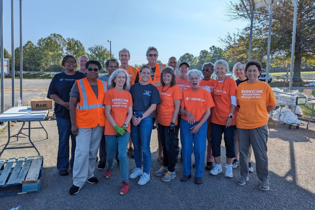 Volunteers are pictured in a group photo at the location of a Mobile Food Pantry. Many wear orange "Everyone should have enough to eat." shirts.