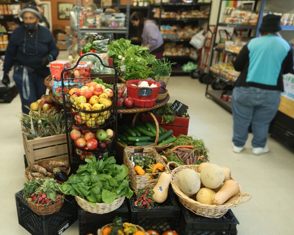 Volunteers and guests fill the small space of River City Bread Basket. A table full of produce takes up the middle of the room.