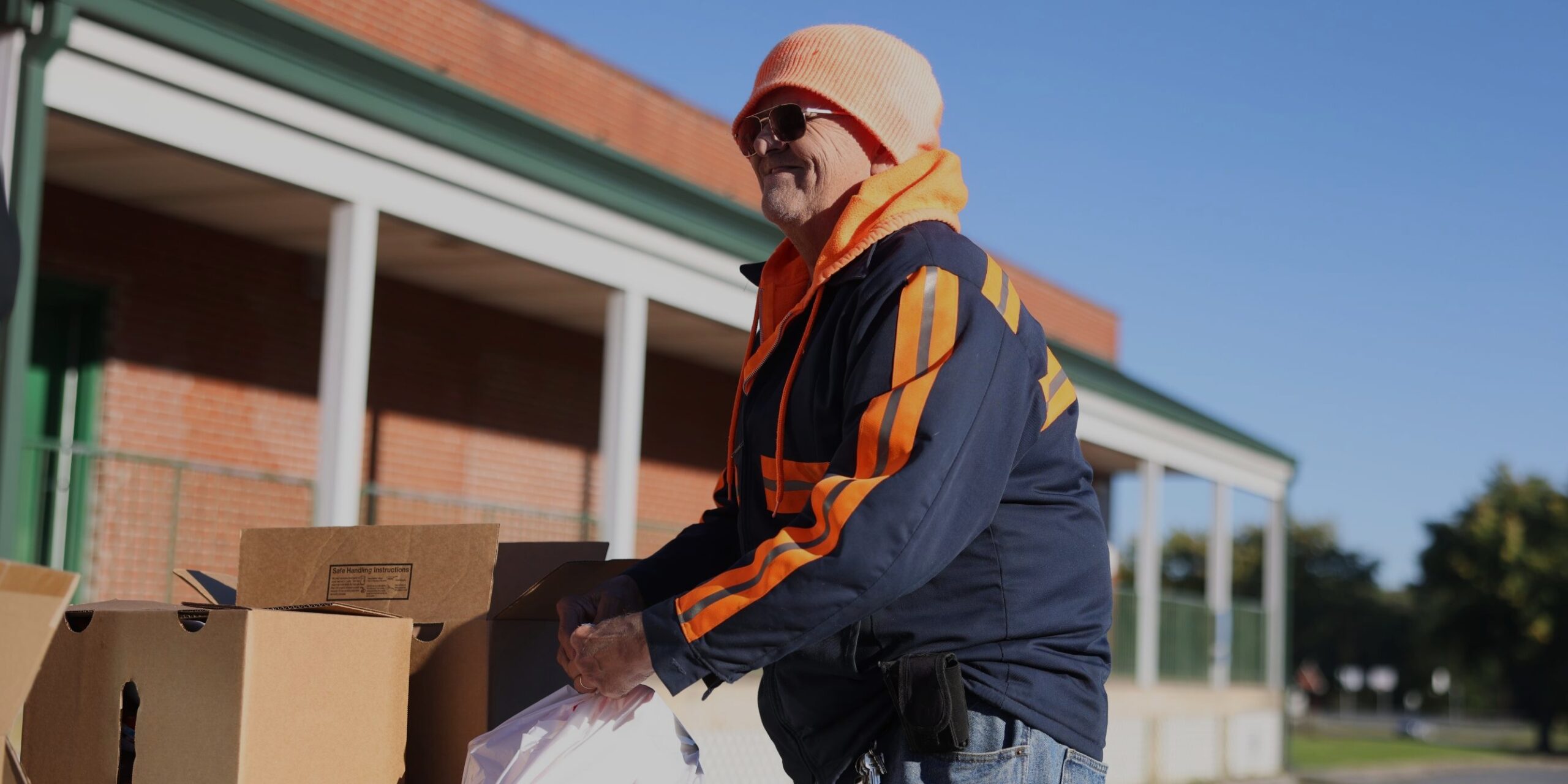 A Mobile Food Pantry Guest lifts a bag of food from a large cardboard box, smiling.