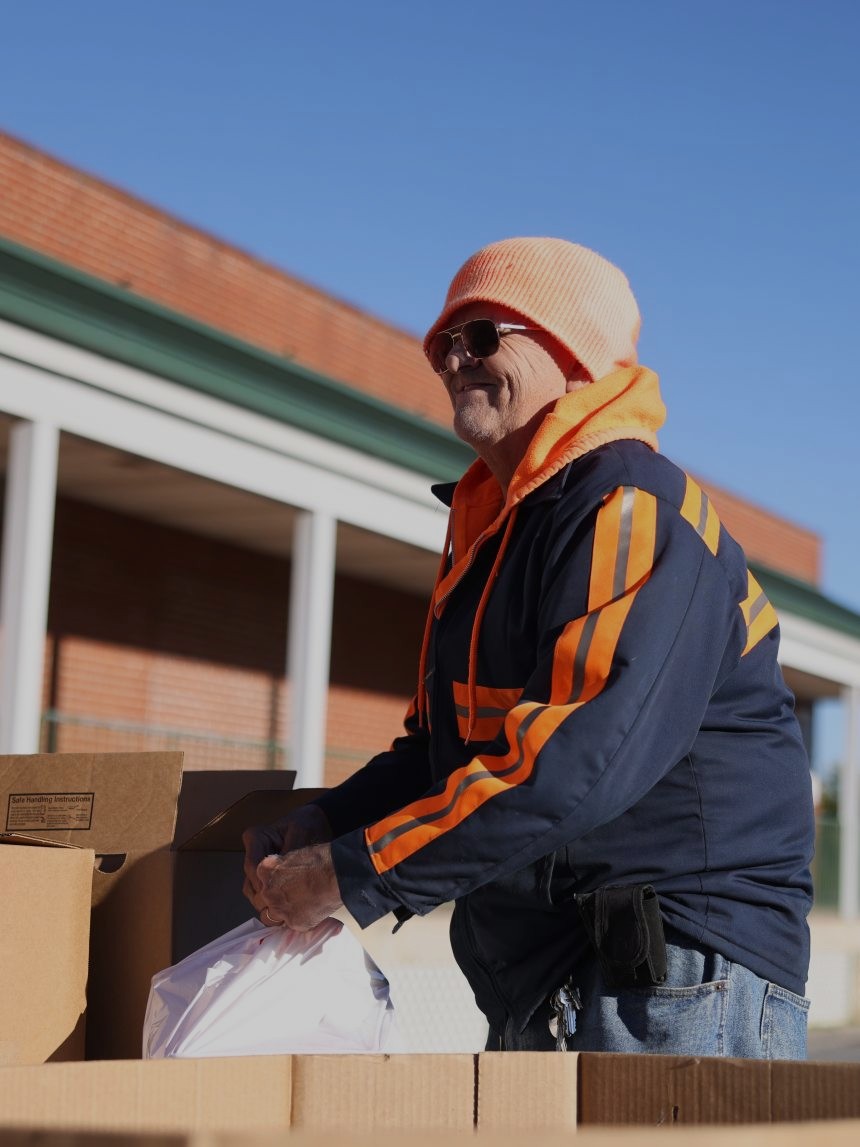 A Mobile Food Pantry Guest lifts a bag of food from a large cardboard box, smiling.