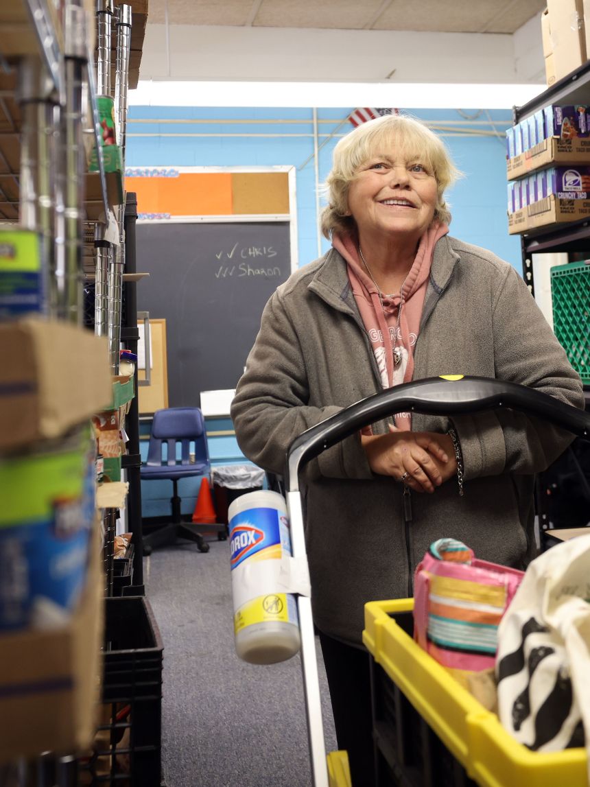 A guest browses the isles of a food pantry, pushing a shopping cart and smiling.