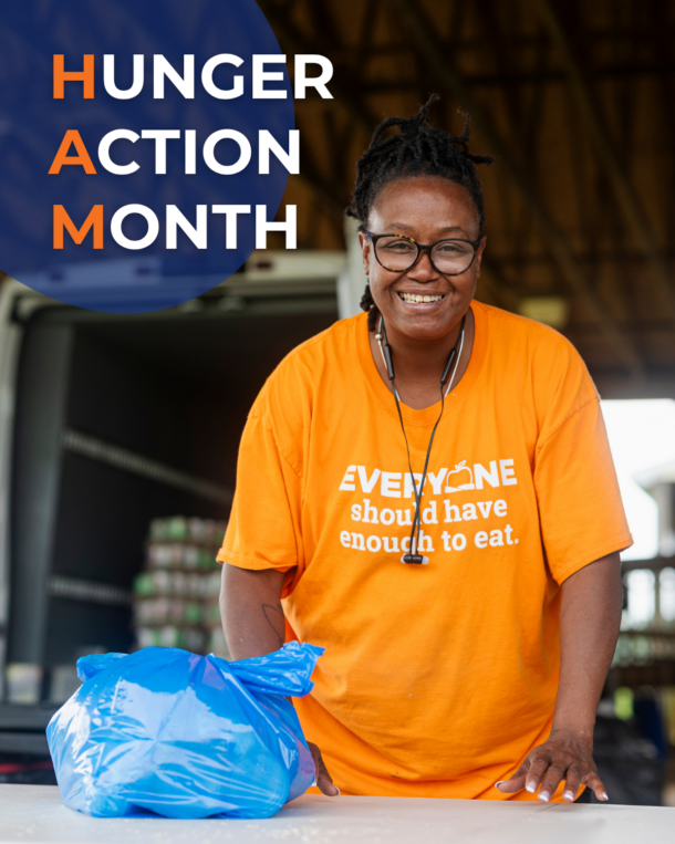 A volunteer wearing an orange, Food Bank branded shirt smiles at the camera. Beside her, there's a bag of food that she's helping pack. She's at a Mobile Food Pantry, a Food Bank Program. "Hunger Action Month" text in the upper left corner.